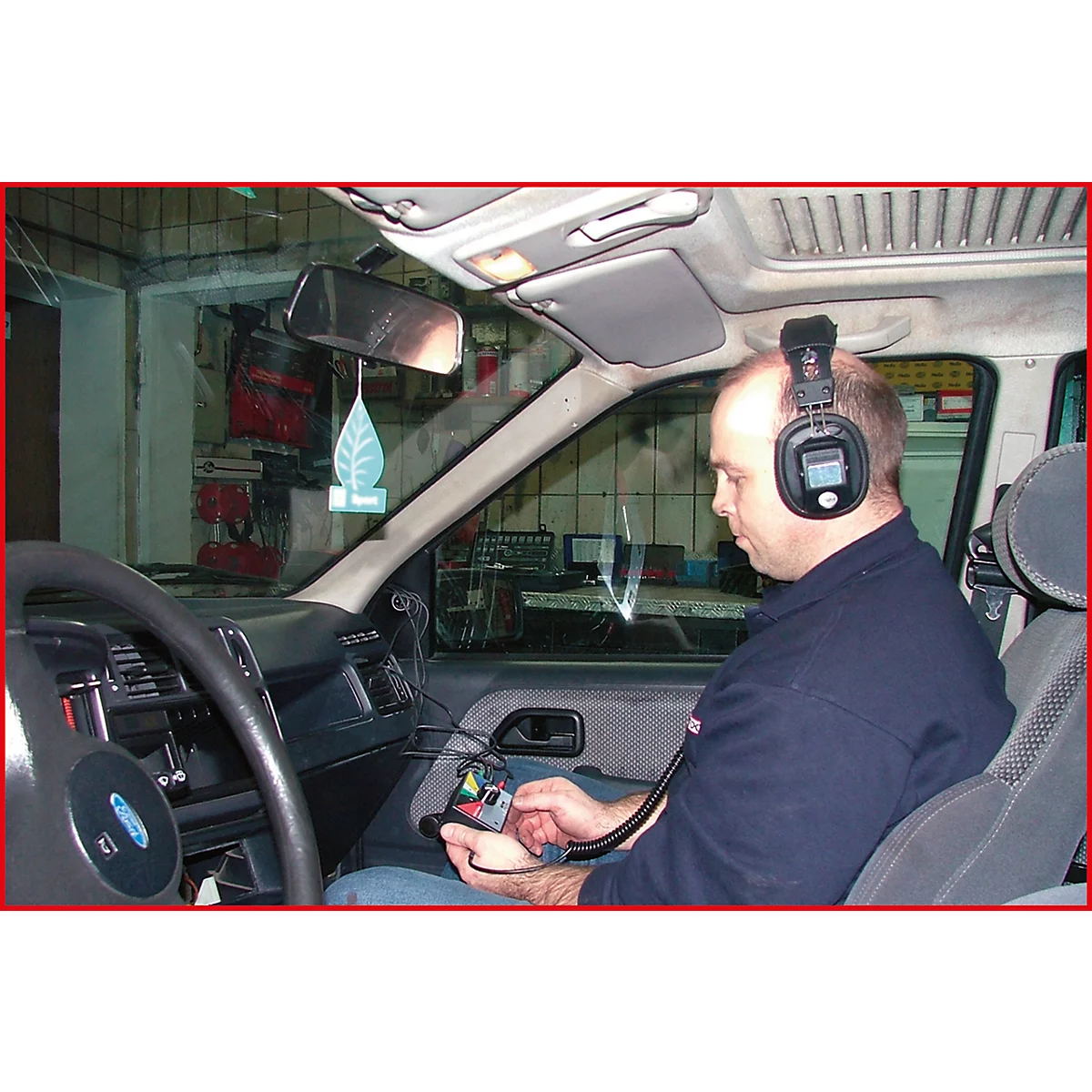 Ein Mann sitzt im Auto mit Kopfhörern und Gerät in der Hand. Vermutlich Fahrzeugdiagnostik.