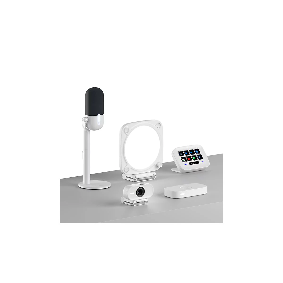 Studio-Setup mit Mikrofon, Webcam, Ringlicht, Bedienfeld und kabelloser Ladevorrichtung, alle weiß. Auf grauer Oberfläche.