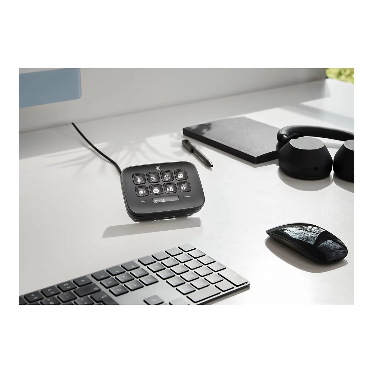 Schwarzes Bedienfeld mit beleuchteten Knöpfen, Kopfhörer, Maus, Tastatur, Notizbuch und Stift auf weißem Tisch.