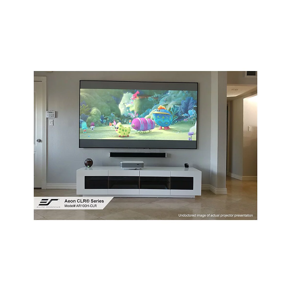GroÃŸer Fernseher mit bunten Zeichentrickfilm-Szenen an einer Wand. Unter dem Fernseher befindet sich ein weiÃŸes Sideboard mit GerÃ¤ten.