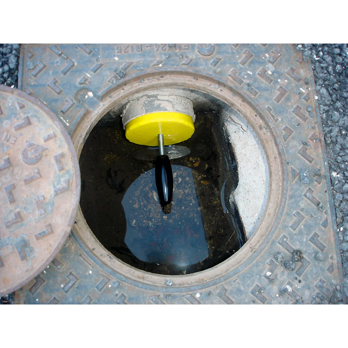 An open manhole cover with a yellow instrument for water level measurement.