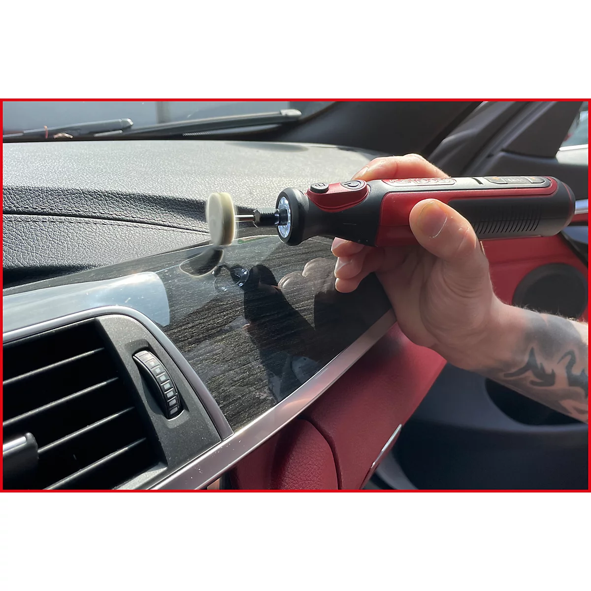 Hand hält rotes, schwarzes Polierwerkzeug im Auto. Es wird auf dem Armaturenbrett verwendet. Tattoo am Arm.