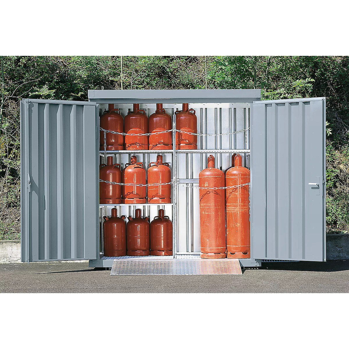 Armoire en acier ouverte avec bouteilles de gaz rouges. Portes ouvertes, bouteilles sécurisées. Arbres à l'extérieur.