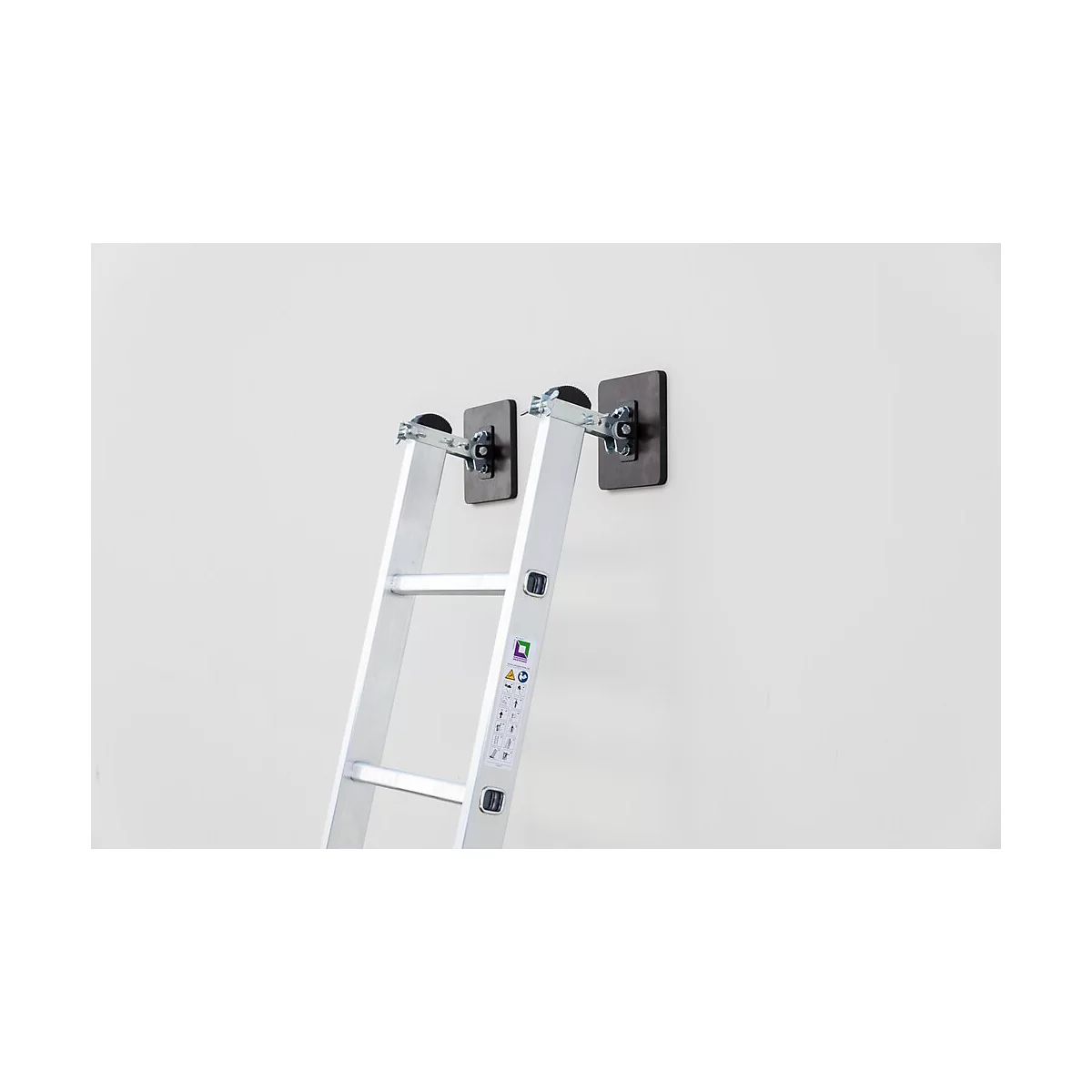 Une échelle en aluminium appuyée contre un mur blanc. Elle est fixée avec deux supports noirs.