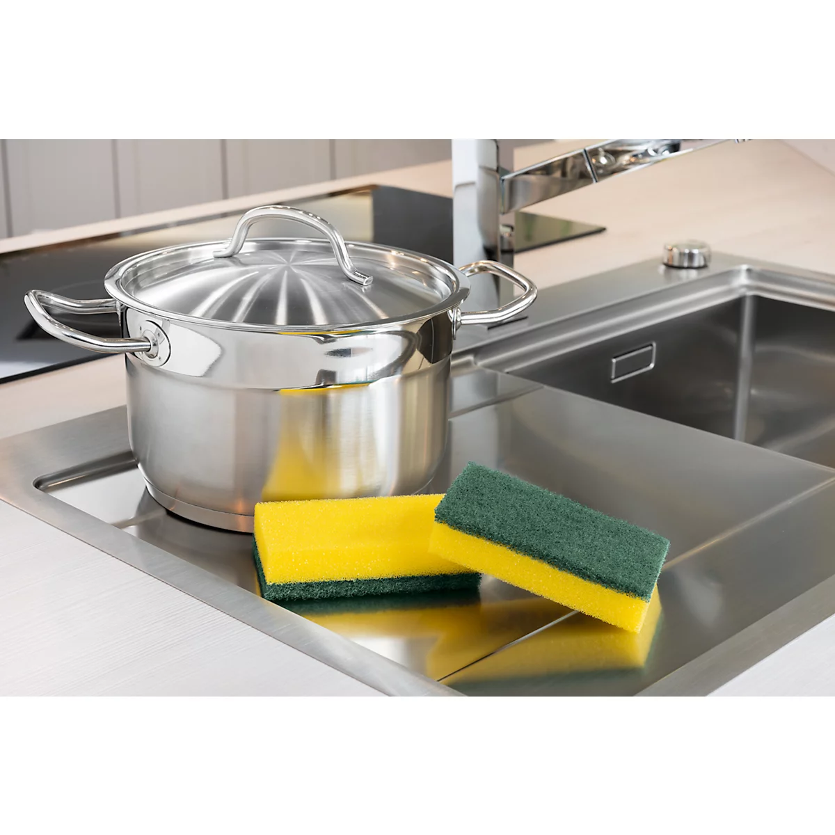 Casserole en acier inoxydable avec couvercle et éponges dans un évier.