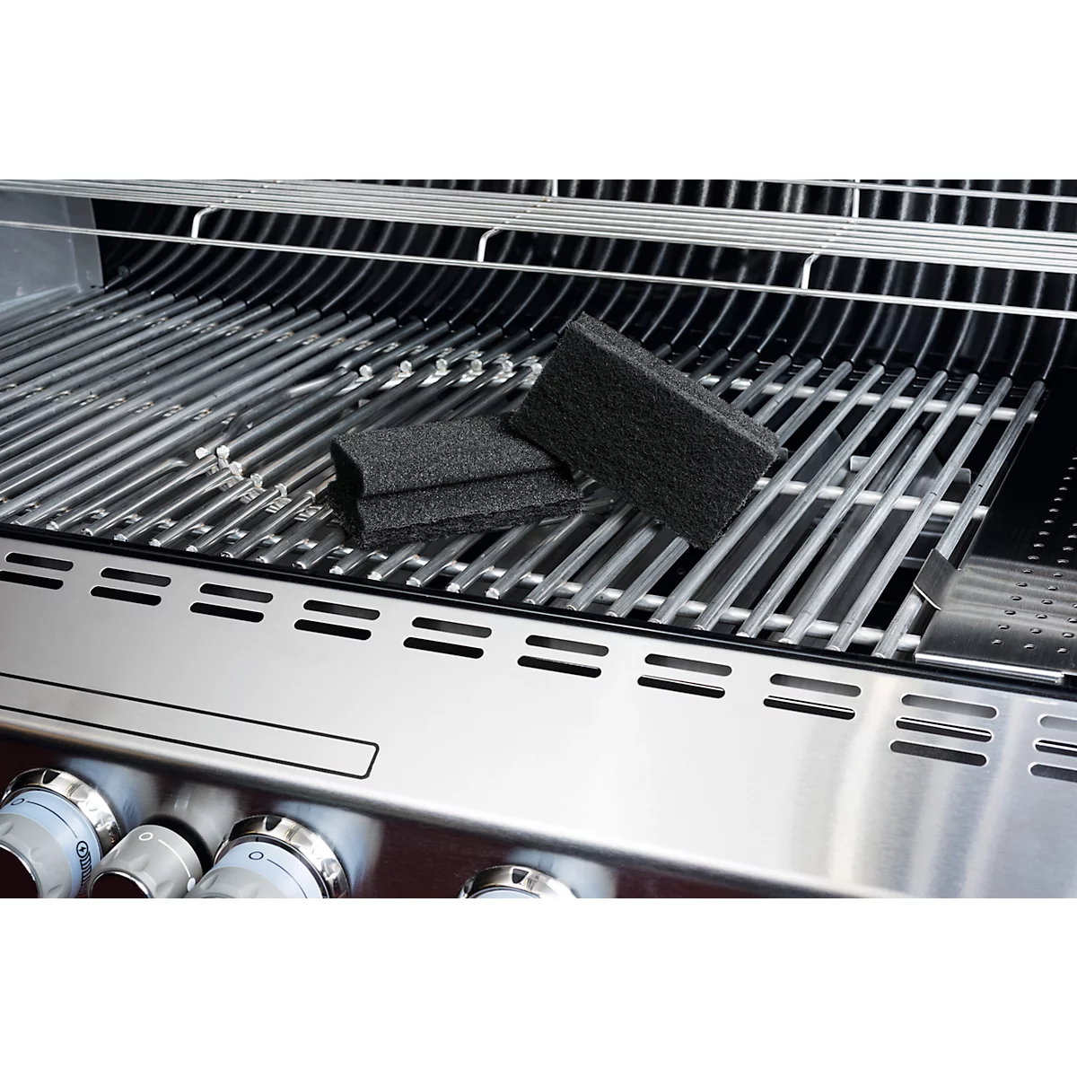 Gros plan sur un barbecue en acier inoxydable. Deux éponges de nettoyage noires sont posées sur la grille du barbecue.
