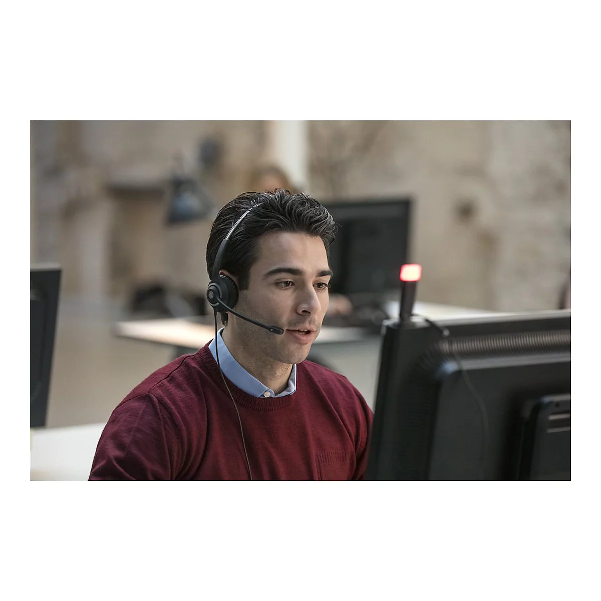 Ein Mann mit Headset sitzt vor einem Computer und spricht.