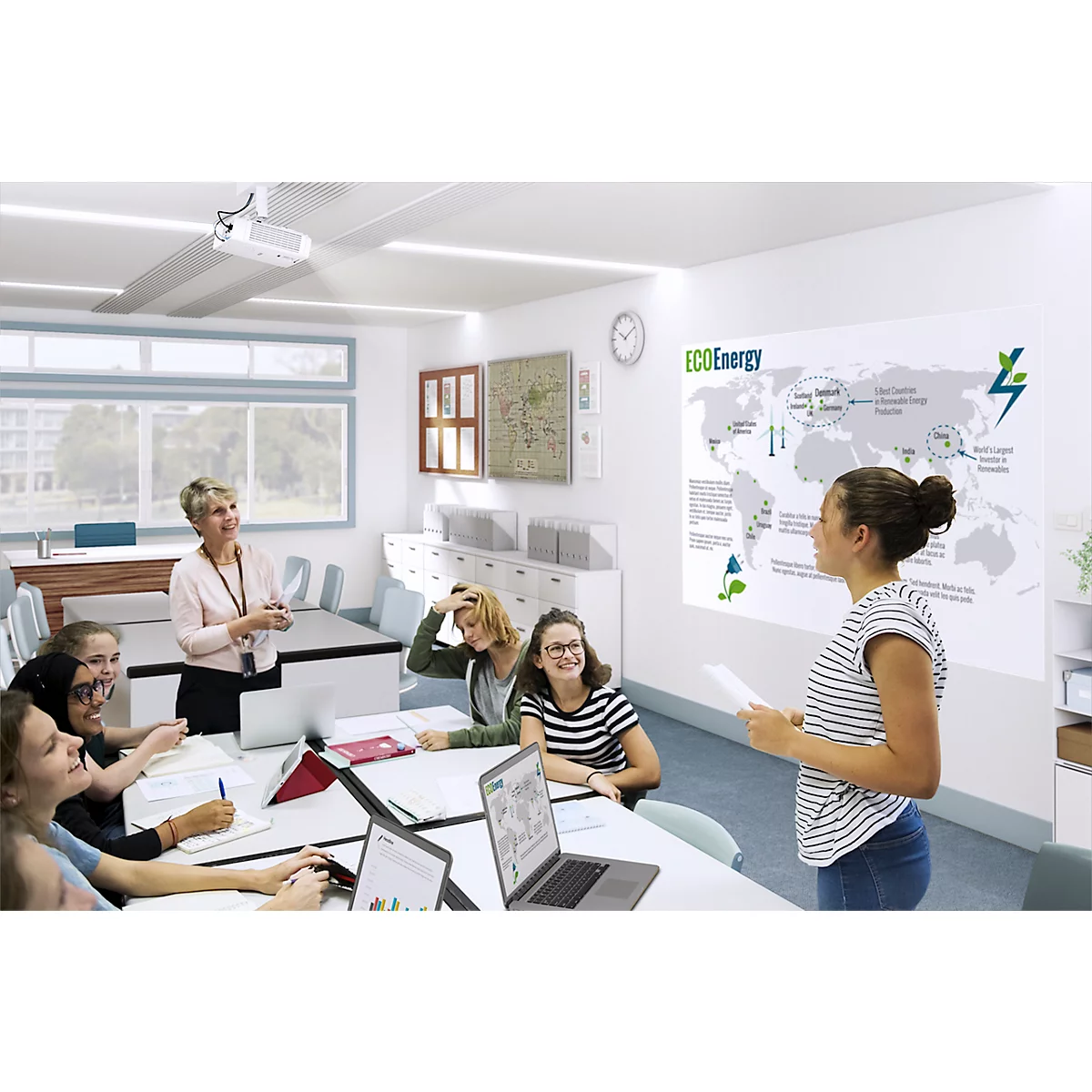 Students listen to a classmate giving a presentation on renewable energy. A projector is in the background.
