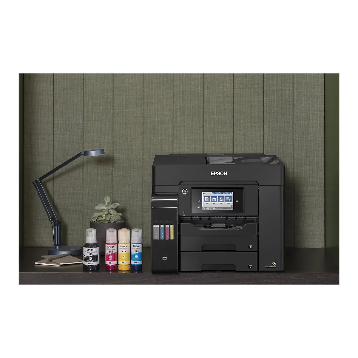 Ein schwarzer Epson-Multifunktionsdrucker steht auf einem Schreibtisch. Vor dem Gerät stehen Tintenflaschen. Links befindet sich eine Schreibtischlampe, rechts ein kleiner Blumentopf.