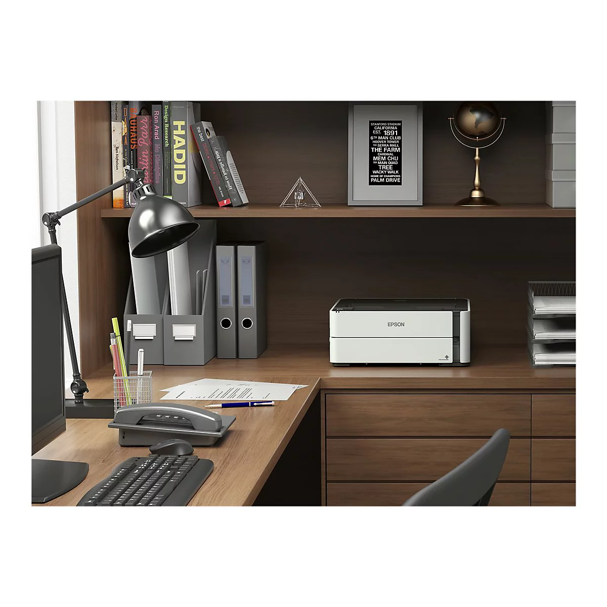 Schreibtisch mit Drucker, Lampe, Telefon und Papier. Im Hintergrund ein Regal mit BÃ¼chern, Ordnern und Dekor.