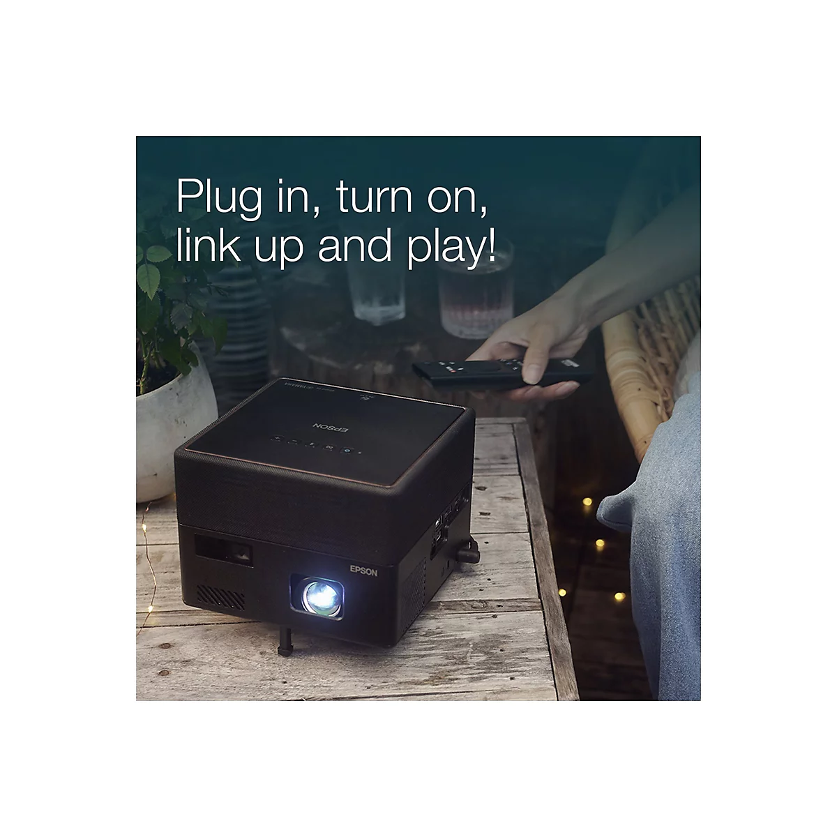 Ein schwarzer Epson-Projektor steht auf einem Holztisch. Darüber steht in weißer Schrift: „Plug in, turn on, link up and play!“. Eine Person hält eine Fernbedienung.