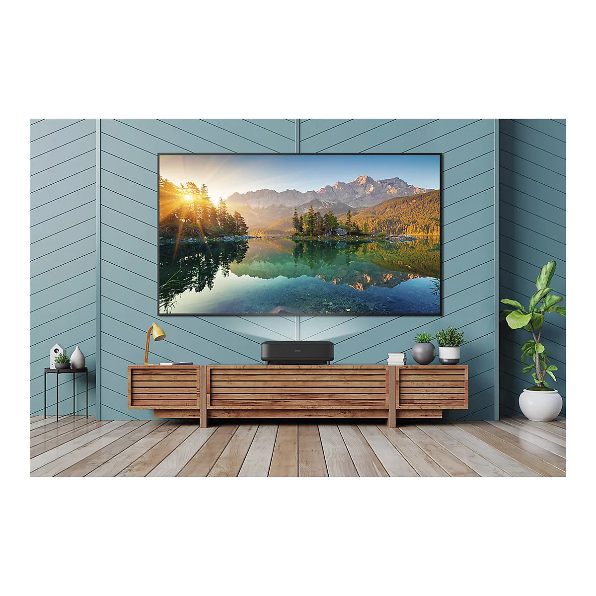Großer Fernseher mit Seelandschaft. Darunter ein schwarzer Projektor auf einem Holzschrank. Zimmer mit Holzboden und grüner Wand.