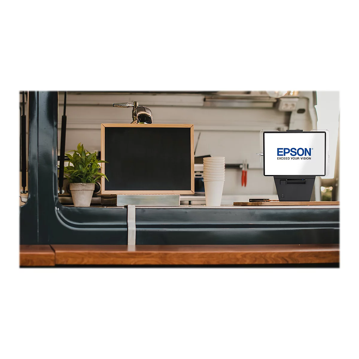 Theke mit Epson-Kassensystem, kleinem Schild, Pflanzen und Bechern. Epson-Logo auf dem Bildschirm.