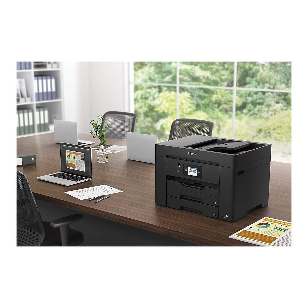 Ein schwarzer Drucker steht auf einem braunen Tisch in einem BÃ¼ro, Laptops und Unterlagen liegen daneben.