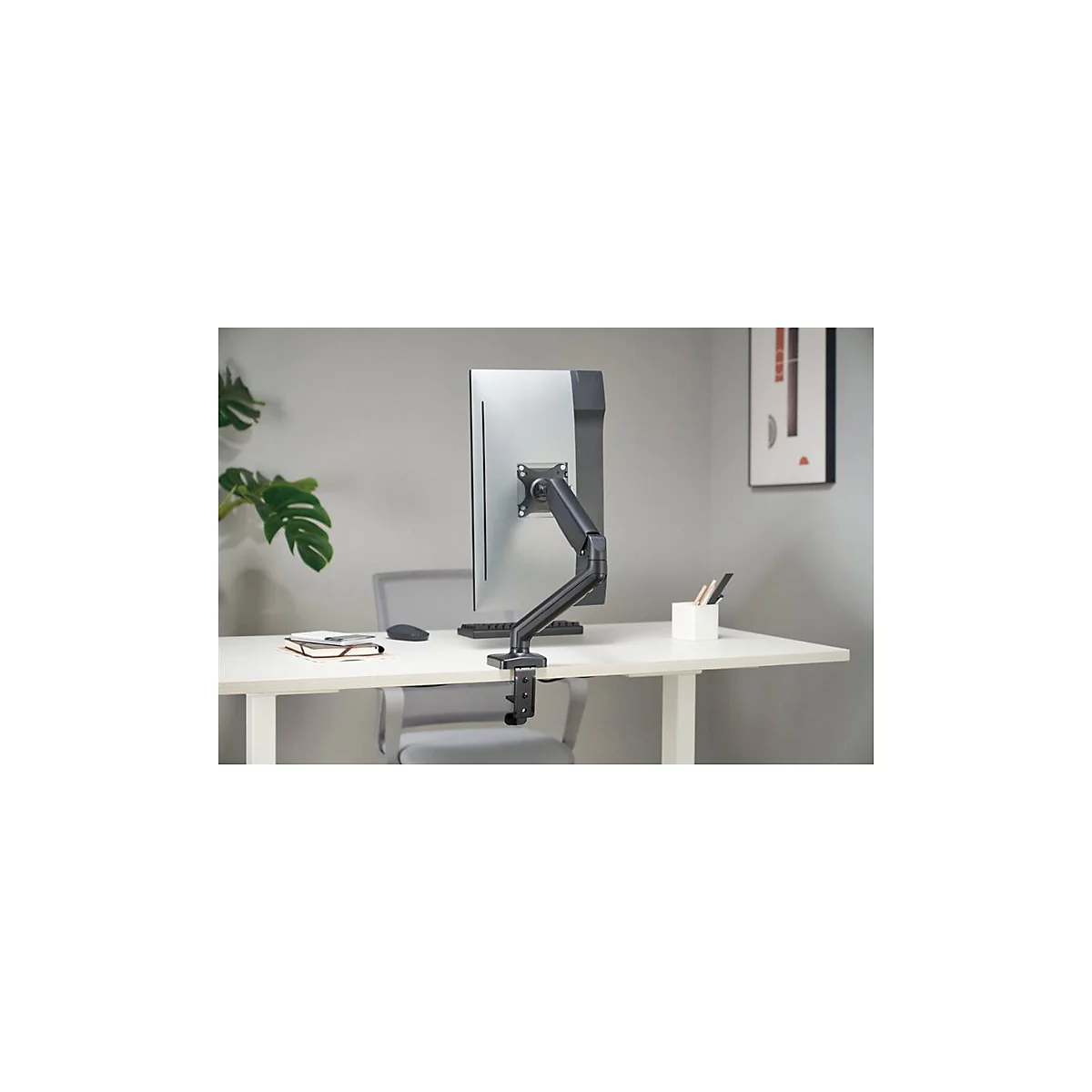 Ein Monitor mit Monitorhalterung, auf einem weiÃŸen Schreibtisch. Im Hintergrund graue Wand und Stuhl.