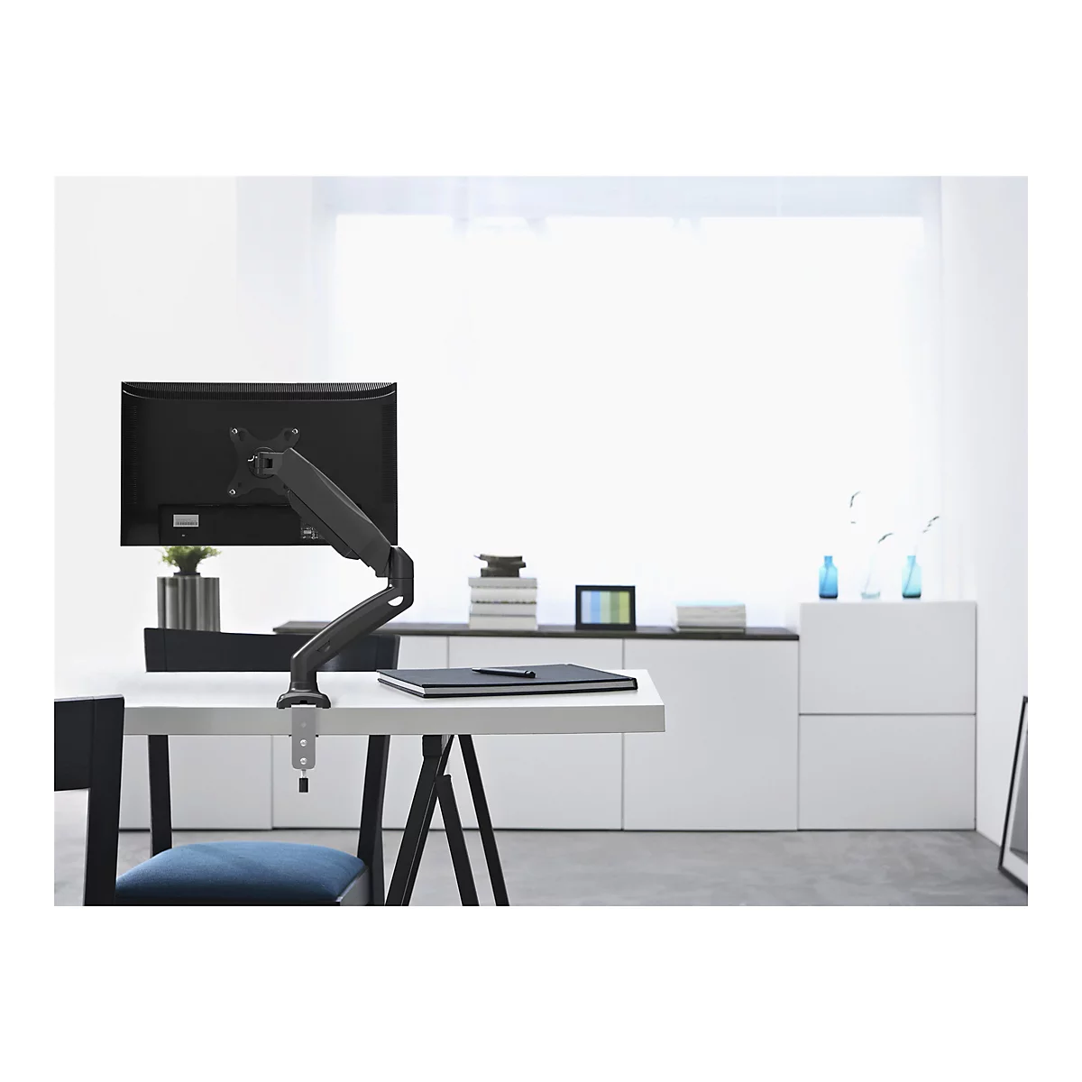 Ein schwarzer Monitor mit Monitorarm steht auf einem weiÃŸen Tisch in einem modernen BÃ¼ro. Hintergrund ist weiÃŸ.
