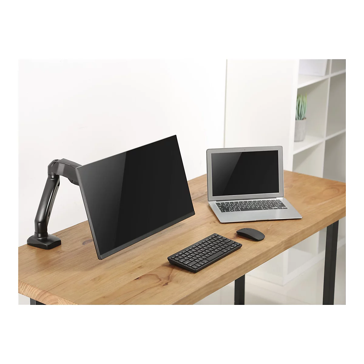 Ein schwarzer Bildschirm an einem Monitorarm steht neben einem Laptop, einer Tastatur und einer Maus auf einem Holzschreibtisch.