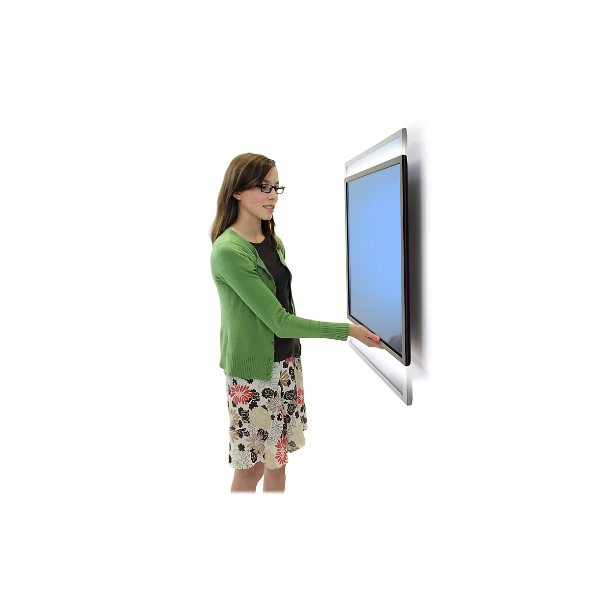 Une jeune femme portant des lunettes touche un écran bleu fixé à un mur. Elle porte un cardigan vert et une jupe à motifs floraux.