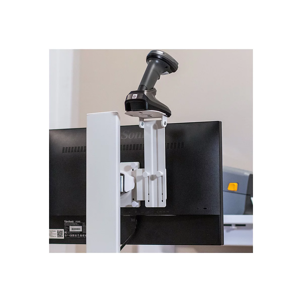 Ein Barcode-Scanner ist an einer weißen Halterung befestigt, die an der Rückseite eines schwarzen Monitors montiert ist.