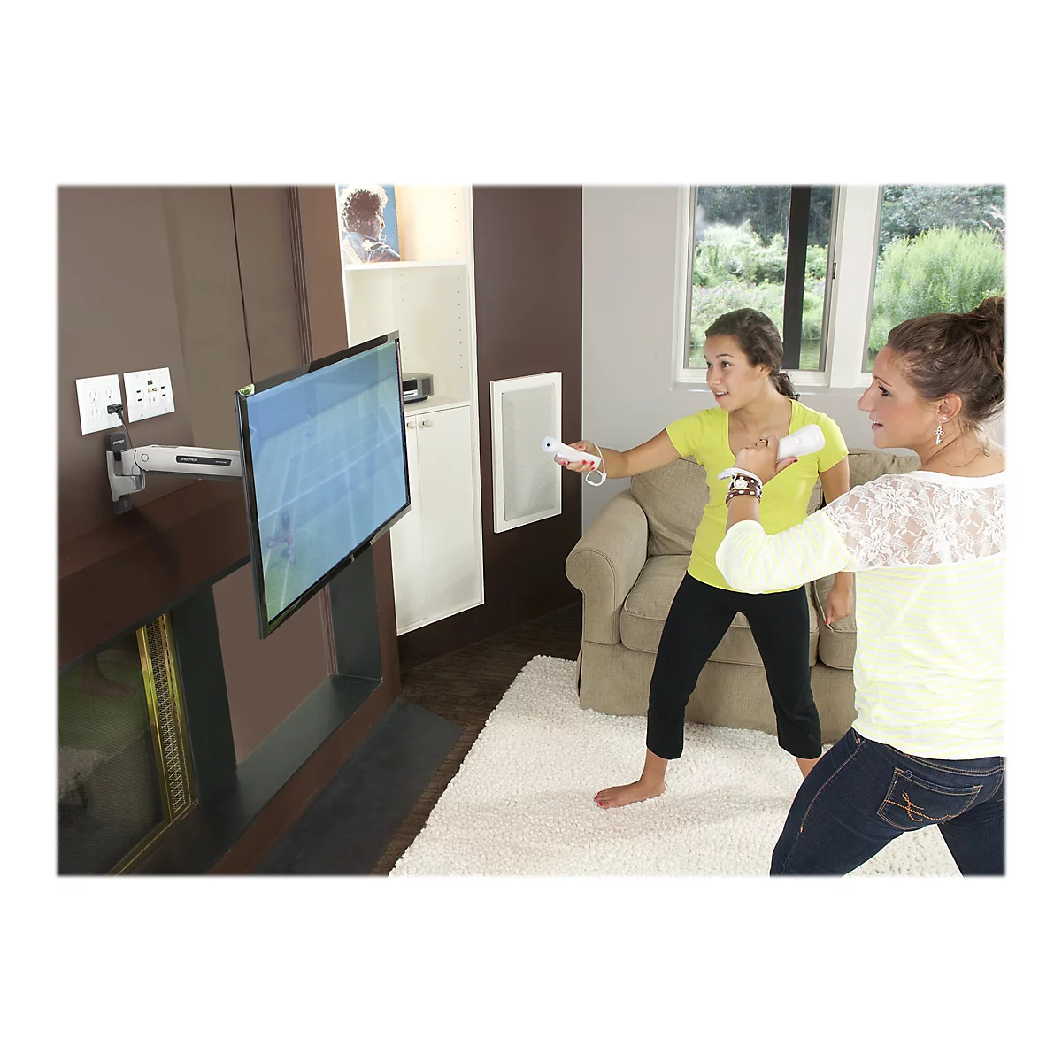Zwei Frauen spielen mit Fernbedienungen vor einem Fernseher ein Videospiel. Beide tragen helle Shirts. Der Fernseher ist an einer Wand montiert.