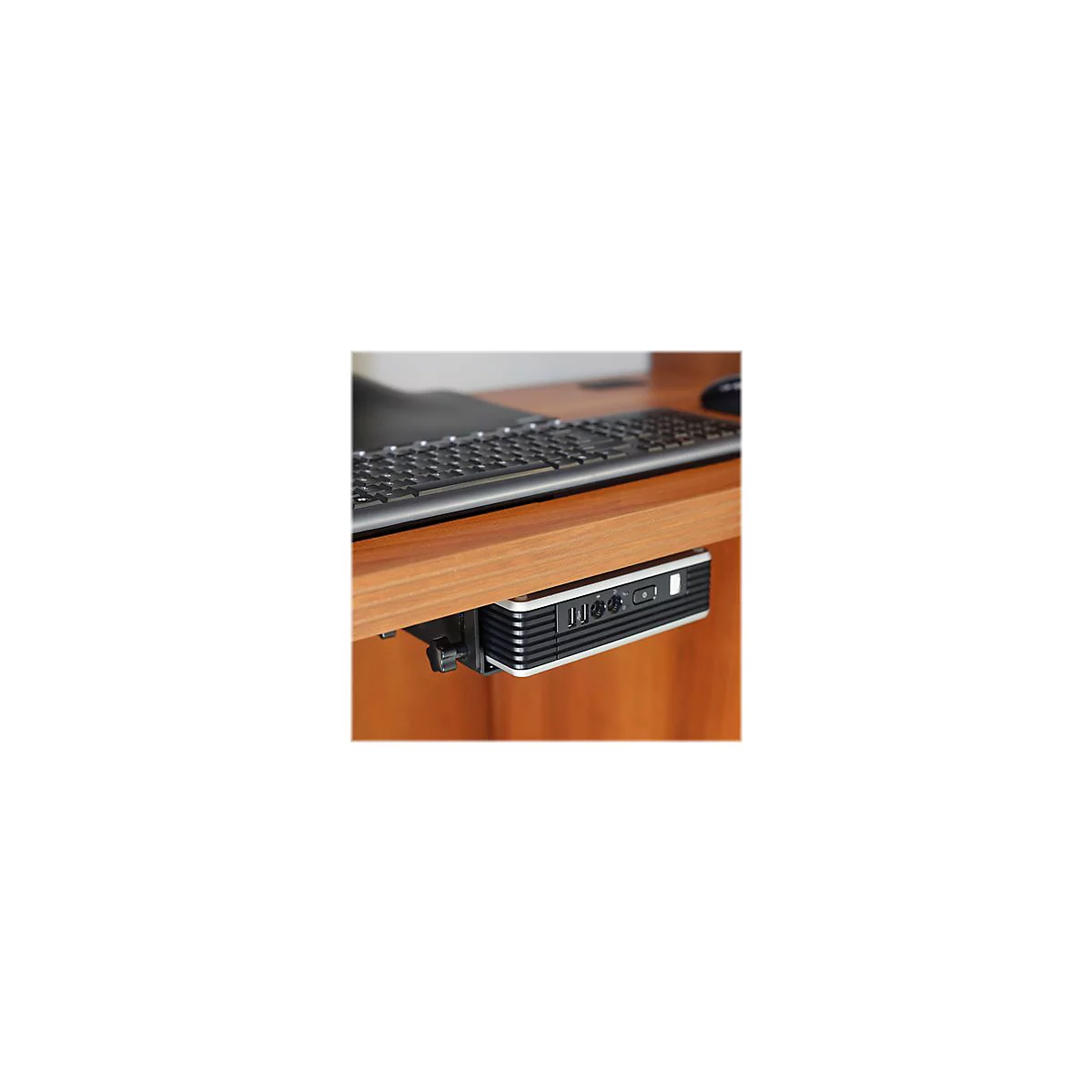 Ein kleiner PC wird unter einem Holzschreibtisch montiert. DarÃ¼ber liegt eine Tastatur.