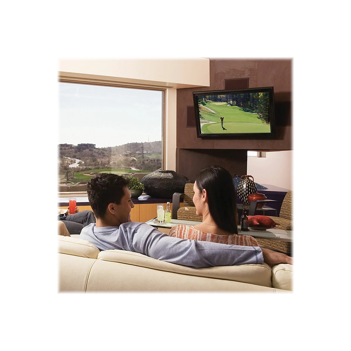 Paar entspannt auf Sofa vor Fernseher. Blick aus Fenster in grÃ¼ne Landschaft. Fernsehbild zeigt Golfer.