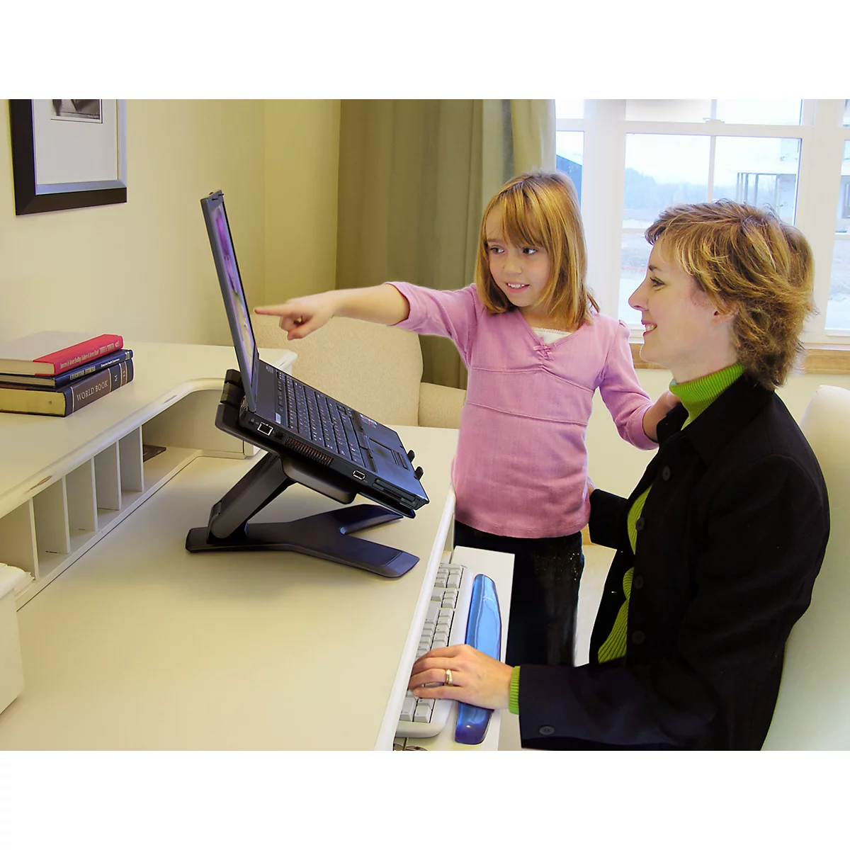 Moeder en kind werken samen op een laptop die op een standaard staat. Het kind wijst naar het scherm.