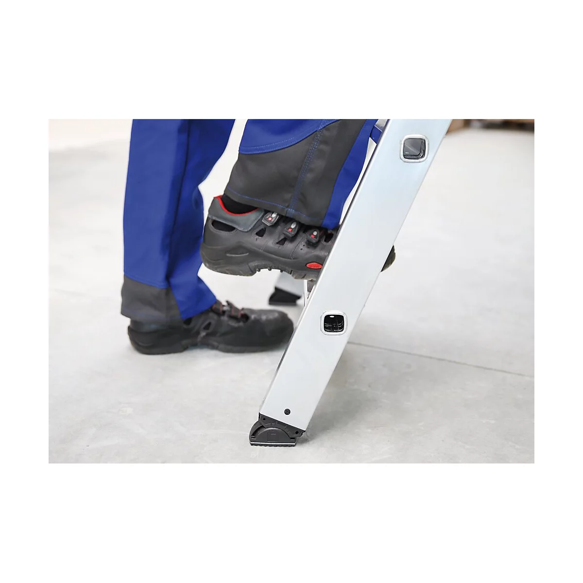 Personne montant sur une échelle. Chaussures de sécurité noires, vêtements de travail bleus. L'échelle est en métal.