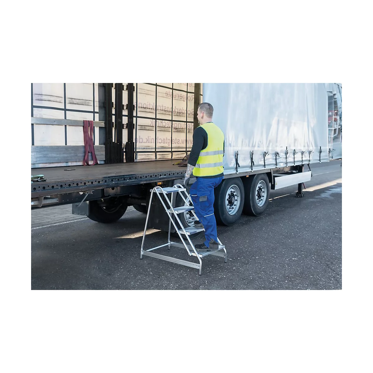 Un homme monte sur un camion à l'aide d'une échelle. Il porte un gilet de sécurité jaune et un pantalon bleu. Le camion a une bâche blanche.