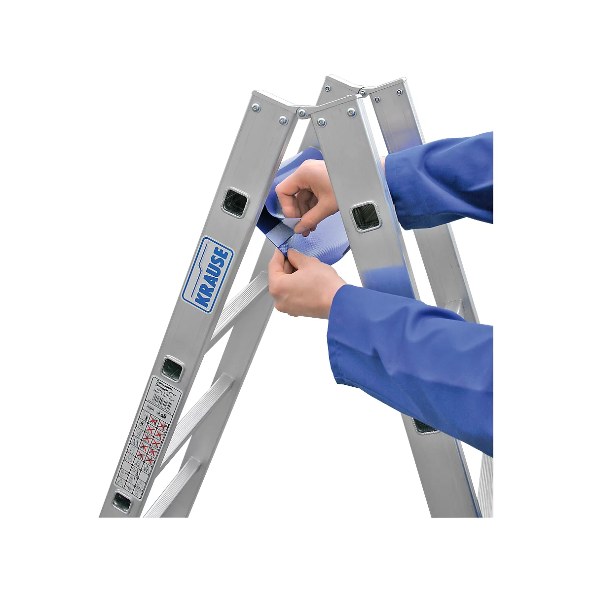 Persona plegando una escalera plateada. Lleva una camisa azul. El producto es de la marca Krause.