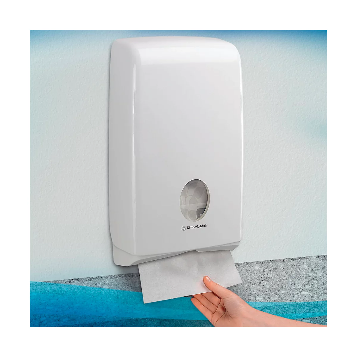 Distributeur d'essuie-mains blanc fixé au mur. Une main prend une serviette en papier.