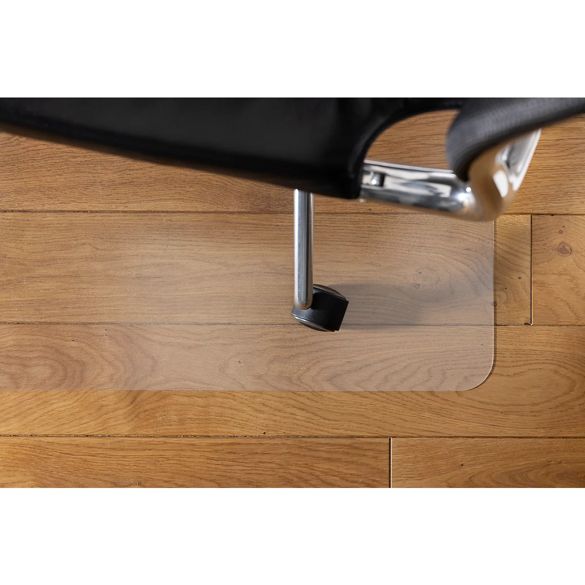 Vista superior de una silla de oficina con asiento negro y patas metálicas de pie sobre una alfombra protectora de suelo transparente en un suelo de madera.
