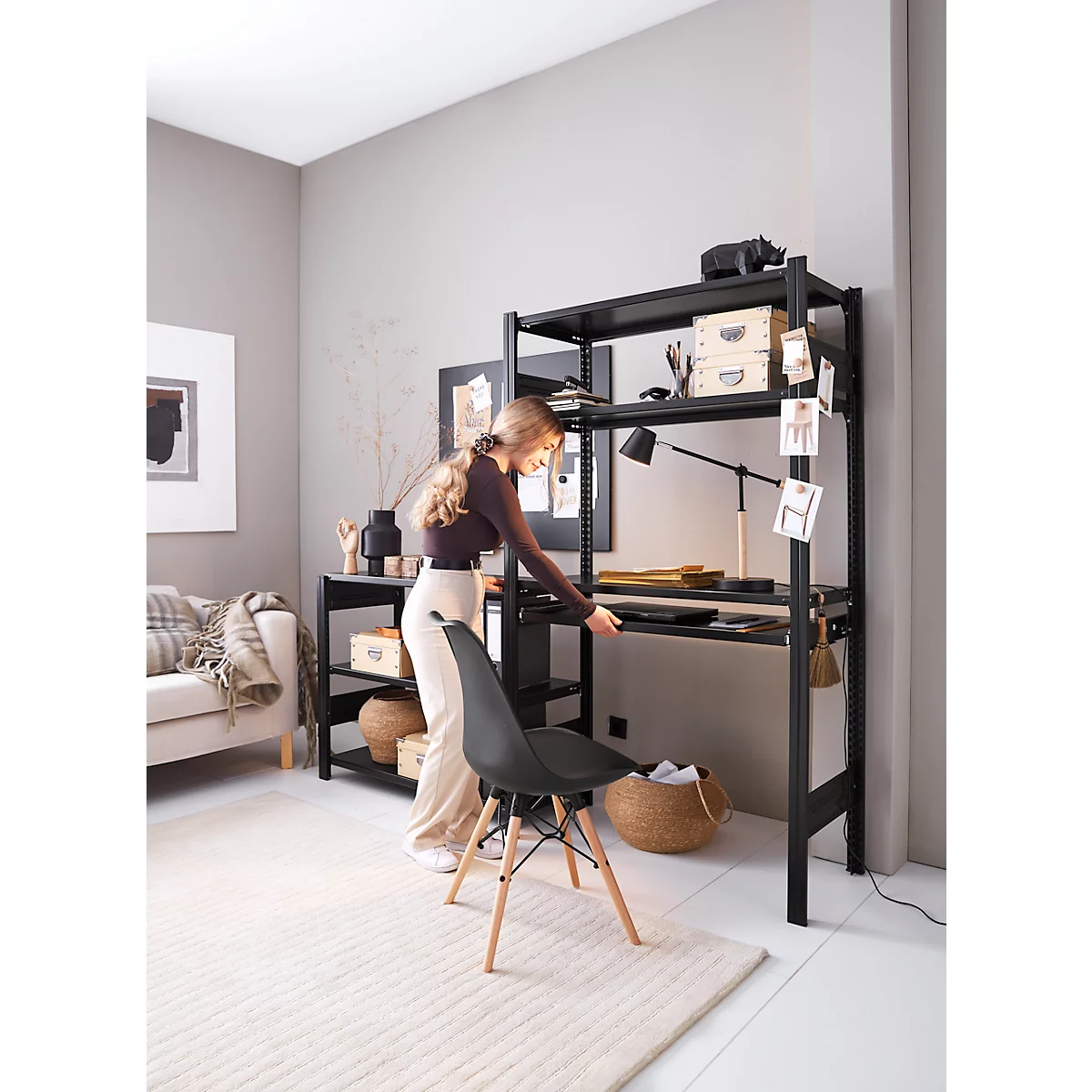 Une femme se tient à un bureau noir avec des étagères, une chaise noire se trouve devant.