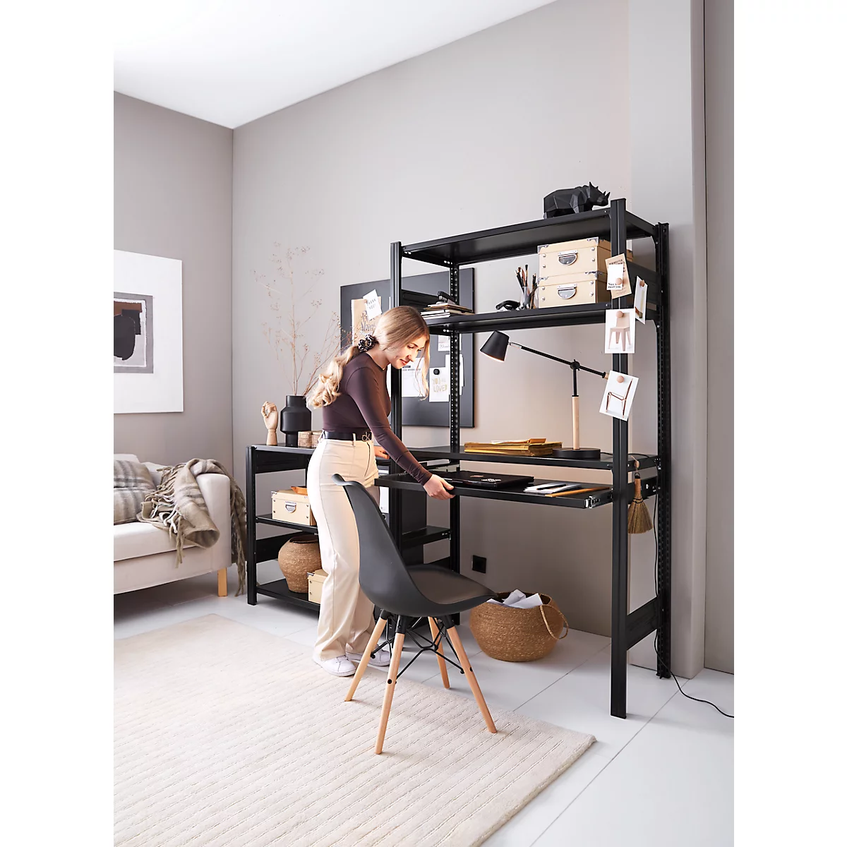 Femme près d'une étagère noire avec bureau, elle place une chaise sur un tapis beige.
