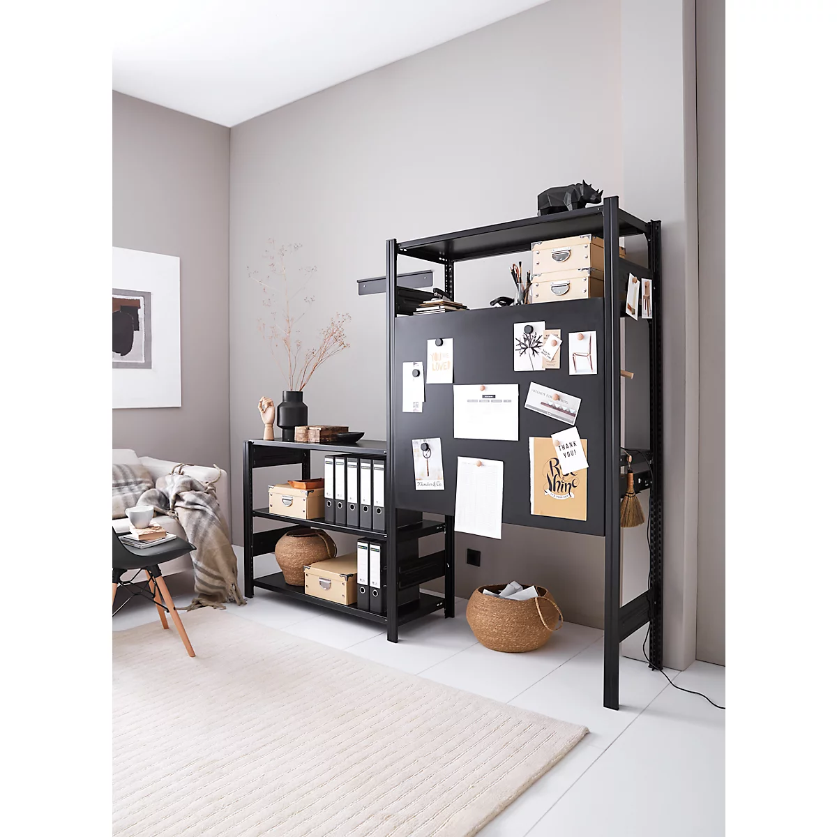 Étagère noire avec un tableau d'affichage, des paniers et des fournitures de bureau. Un tapis crème au sol. Une œuvre d'art est accrochée au mur.