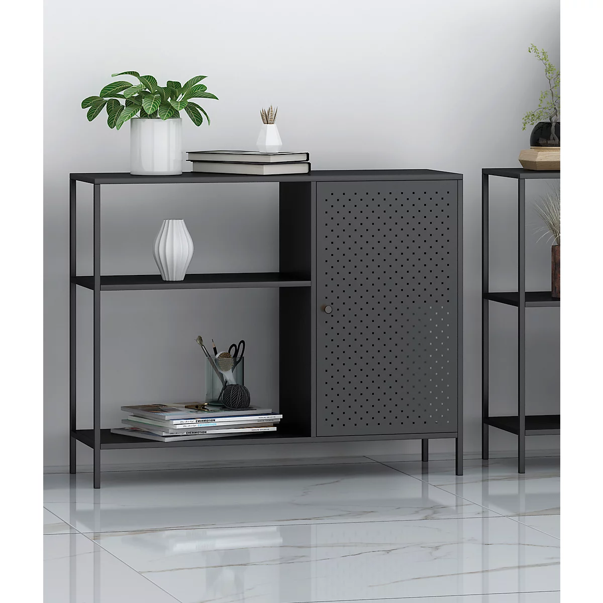Étagère en métal gris avec porte perforée et décoration. Une étagère d'appoint se dresse devant un mur blanc.