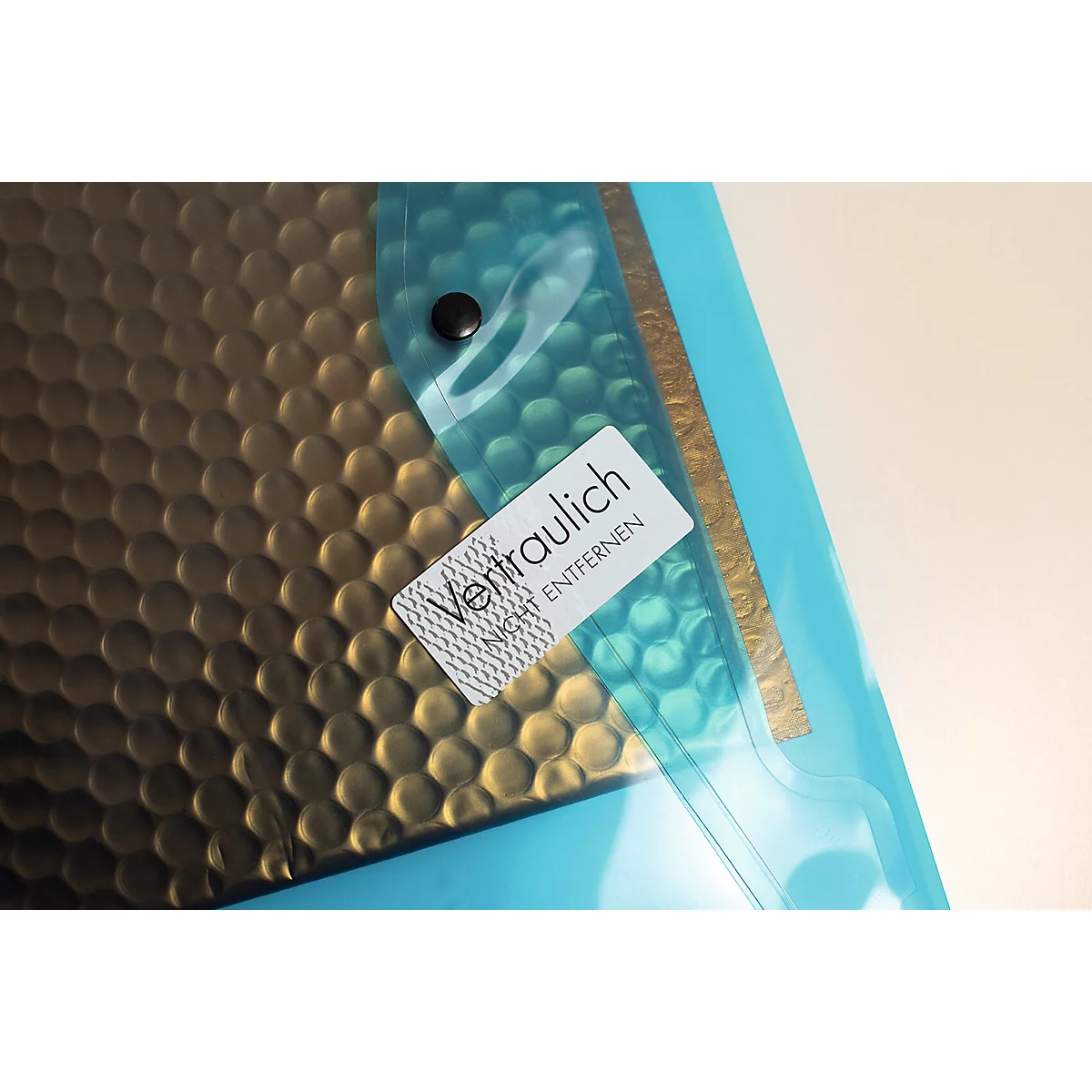 Pochette de documents bleu et or, avec une étiquette indiquant "Confidentiel". Un bouton noir maintient le film transparent.