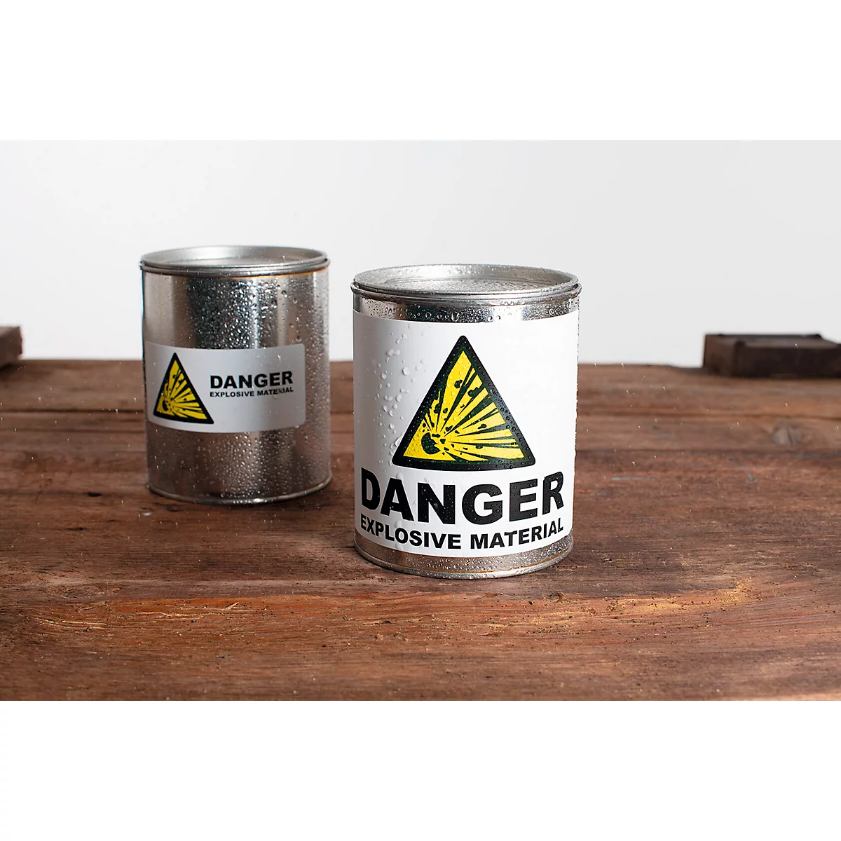 Deux boîtes argentées avec des étiquettes "danger" sur une planche en bois.