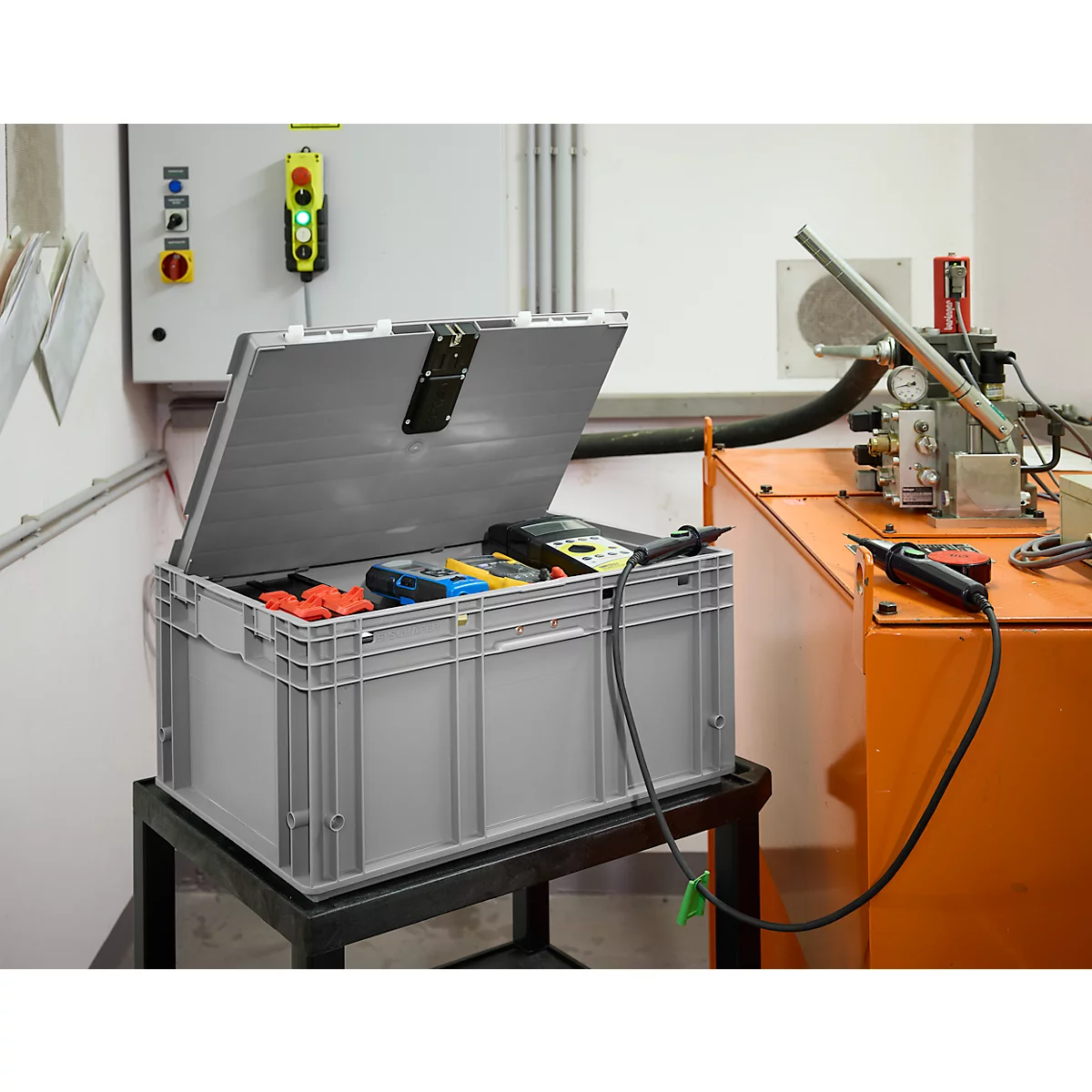 Grijze gereedschapskist met open deksel, gevuld met gereedschap. Technische apparatuur en een schakelpaneel op de achtergrond.