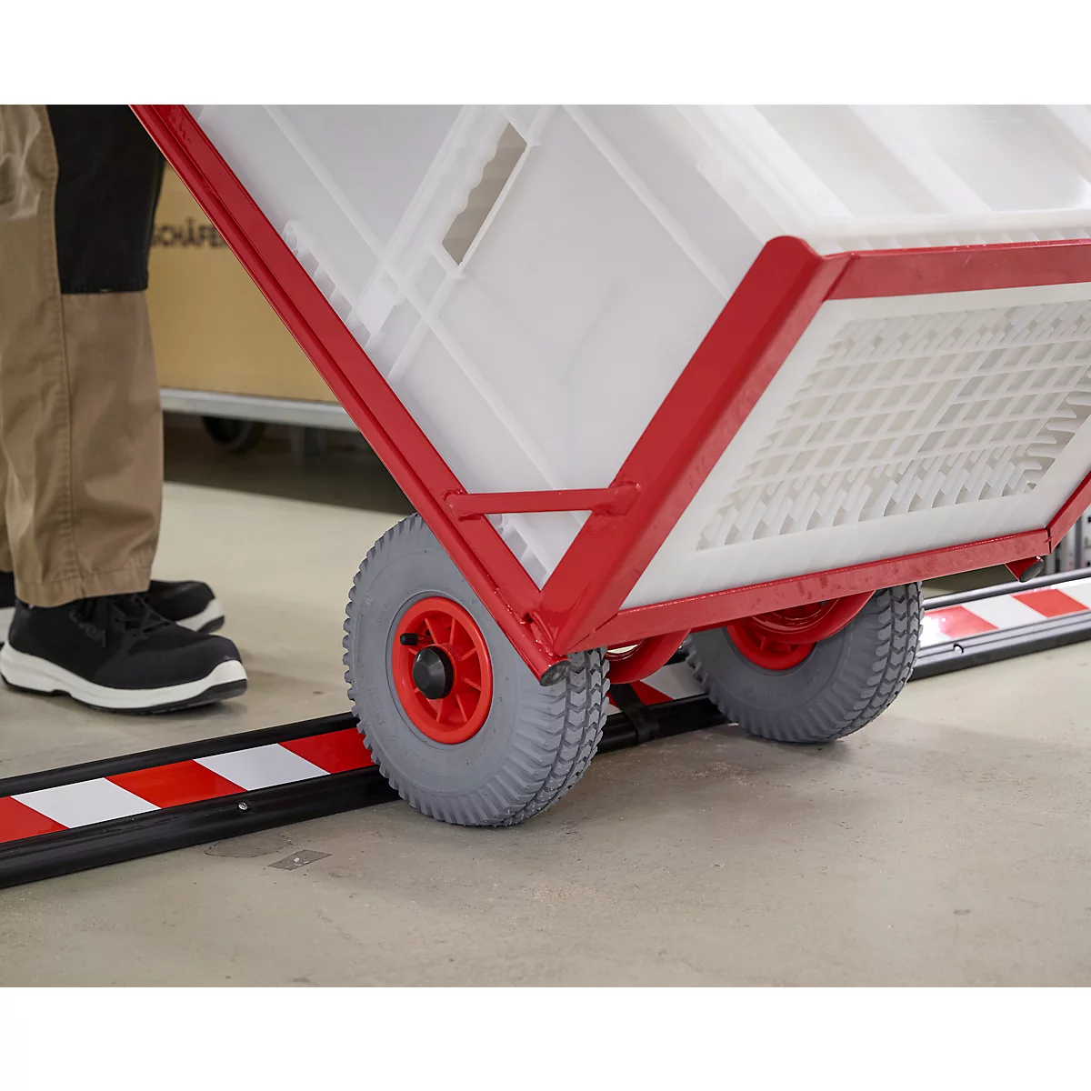 Nahaufnahme eines roten, rollbaren Transporters. Graue Reifen fahren über eine rot-weiß gestreifte Schiene.