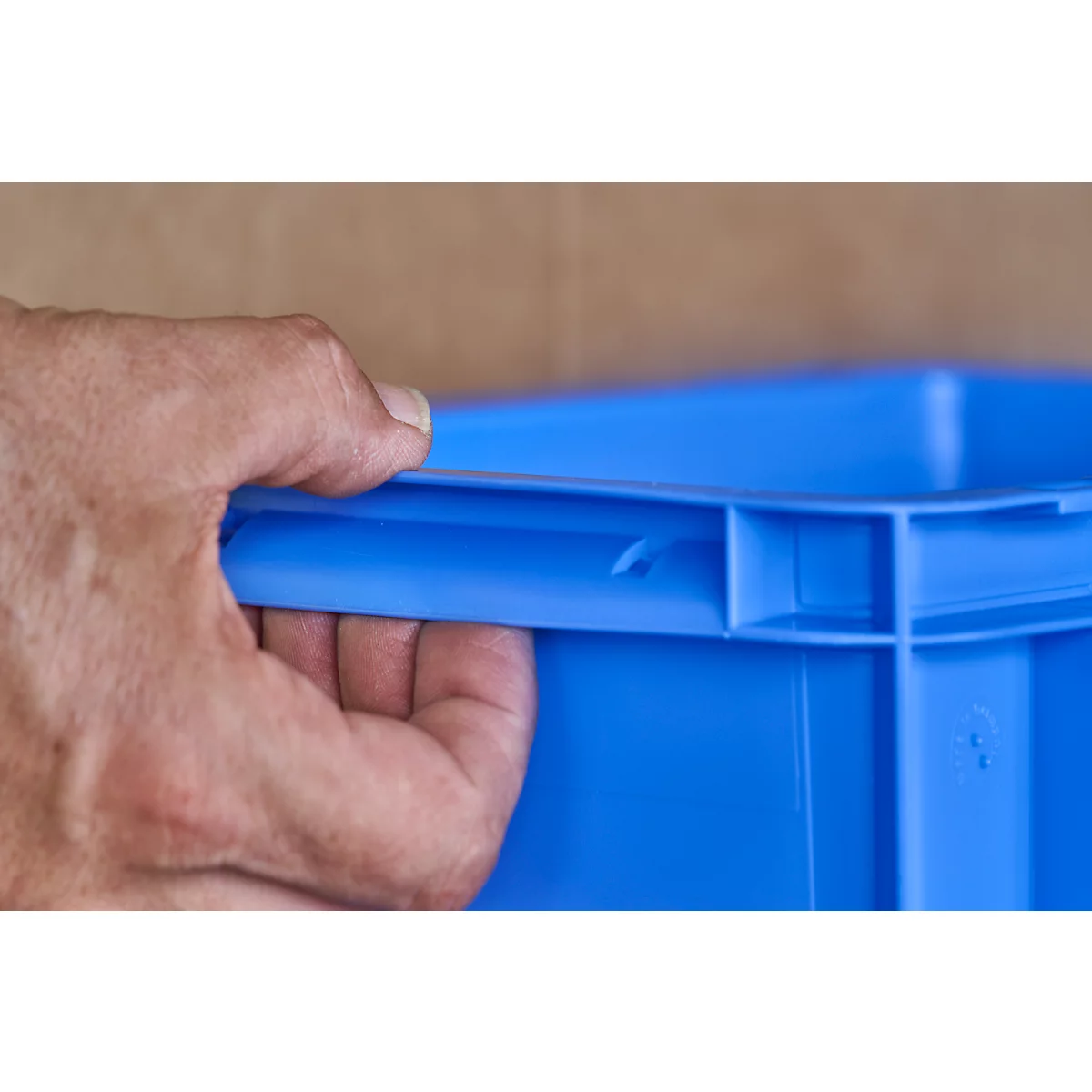 Close-up of a hand holding a blue plastic box by the handle.
