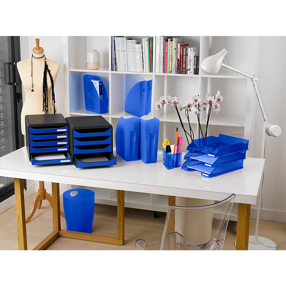 Schreibtisch mit Büromaterialien: blaue Briefablagen, Ordner, Stifte und ein Stehpult.
