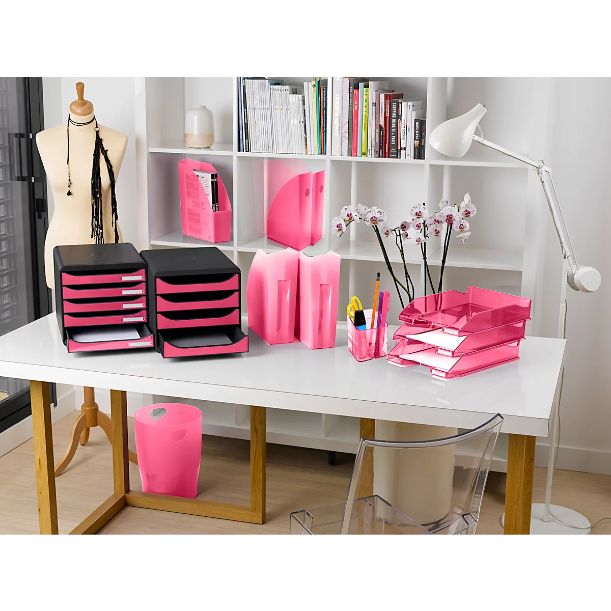 Ein Schreibtisch mit pinkfarbenem Bürobedarf, darunter Ablagen, Stifthalter, Papierkörbe und Ordner. Eine Orchidee steht daneben.