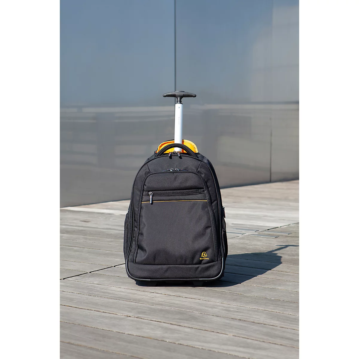 Schwarzer Trolley-Rucksack mit ausziehbarem Griff. Auf grauem Holz. Gelbes Detail am oberen Ende.