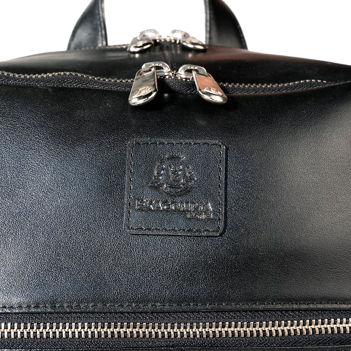 Detailaufnahme einer schwarzen Ledertasche mit Reißverschluss, silbernen Zippern und einem Leder-Label.