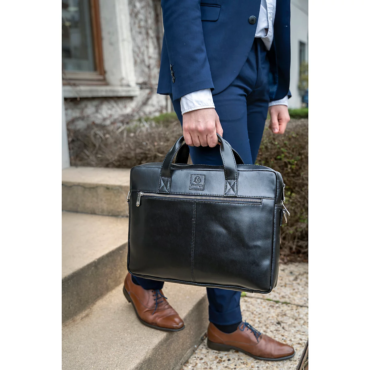 Ein Mann in blauem Anzug und Lederschuhen trägt eine schwarze Aktentasche die Treppe hinunter.