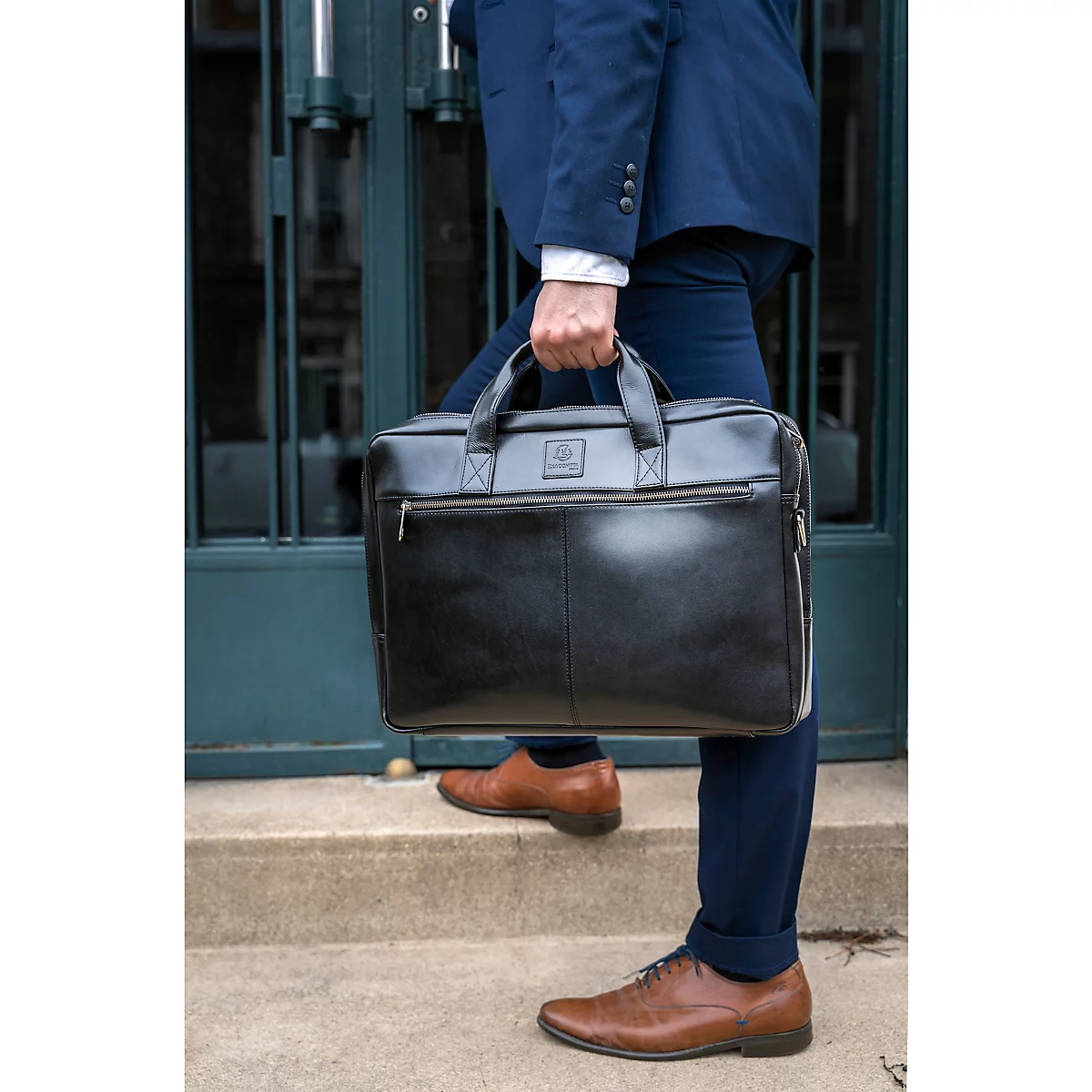 Un homme en costume tient une serviette noire. Il monte les escaliers. Chaussures en cuir marron.