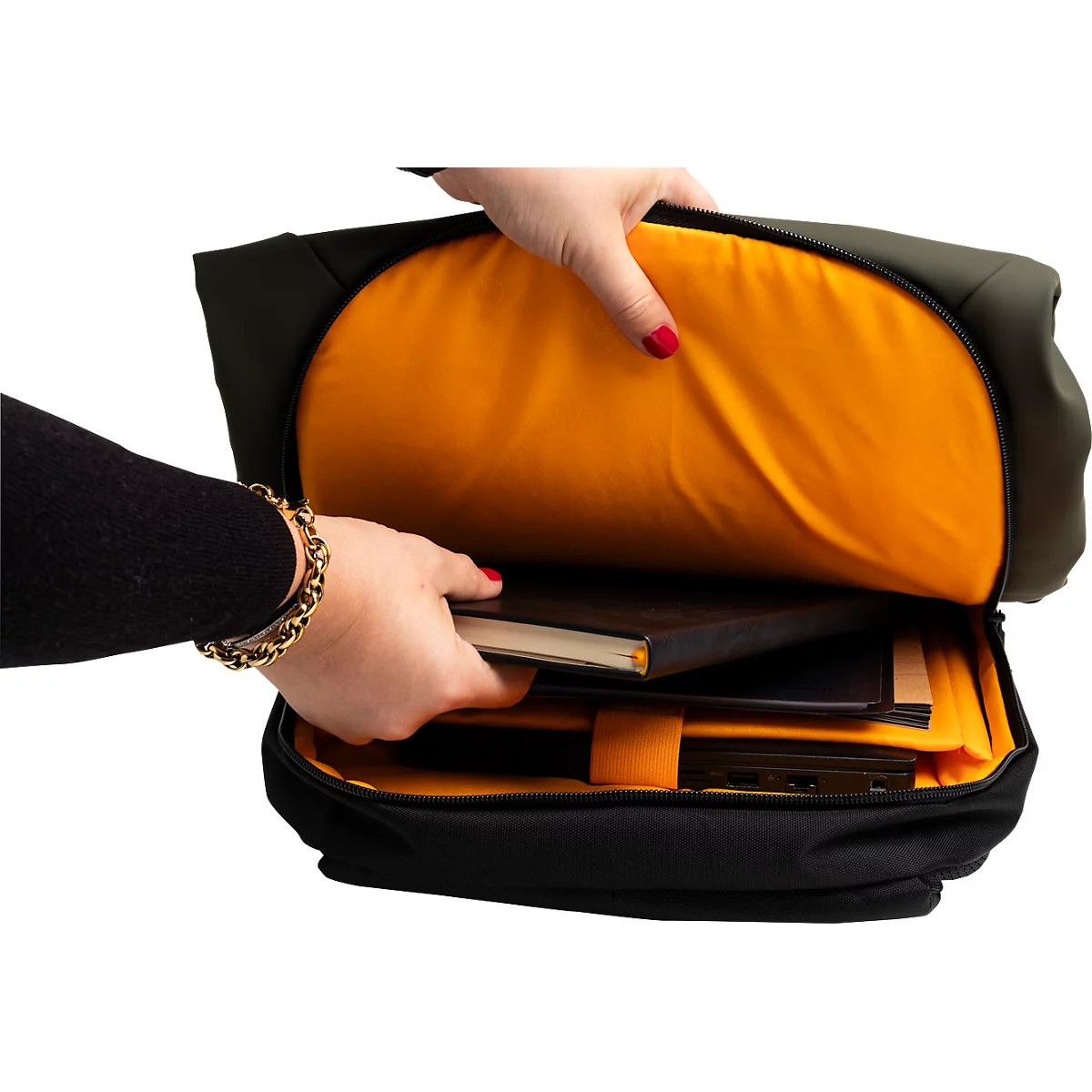 Person öffnet schwarzen Rucksack mit orangefarbener Innenausstattung. Hält Notizbücher, rote Fingernägel und Armband sichtbar.