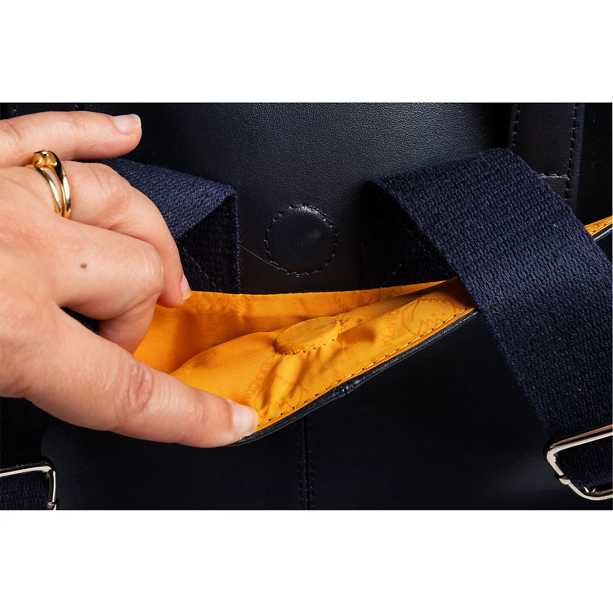 Gros plan d'une main atteignant la poche intérieure jaune d'un sac à dos bleu marine.