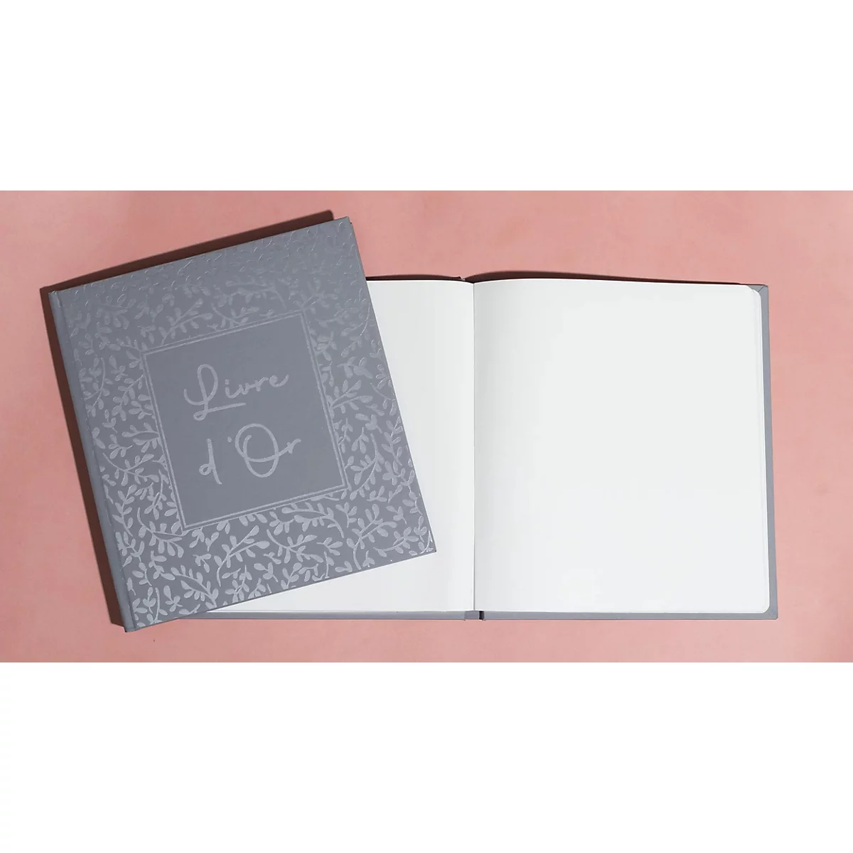 Livre gris intitulé 'Livre d'Or' posé ouvert sur fond rose.